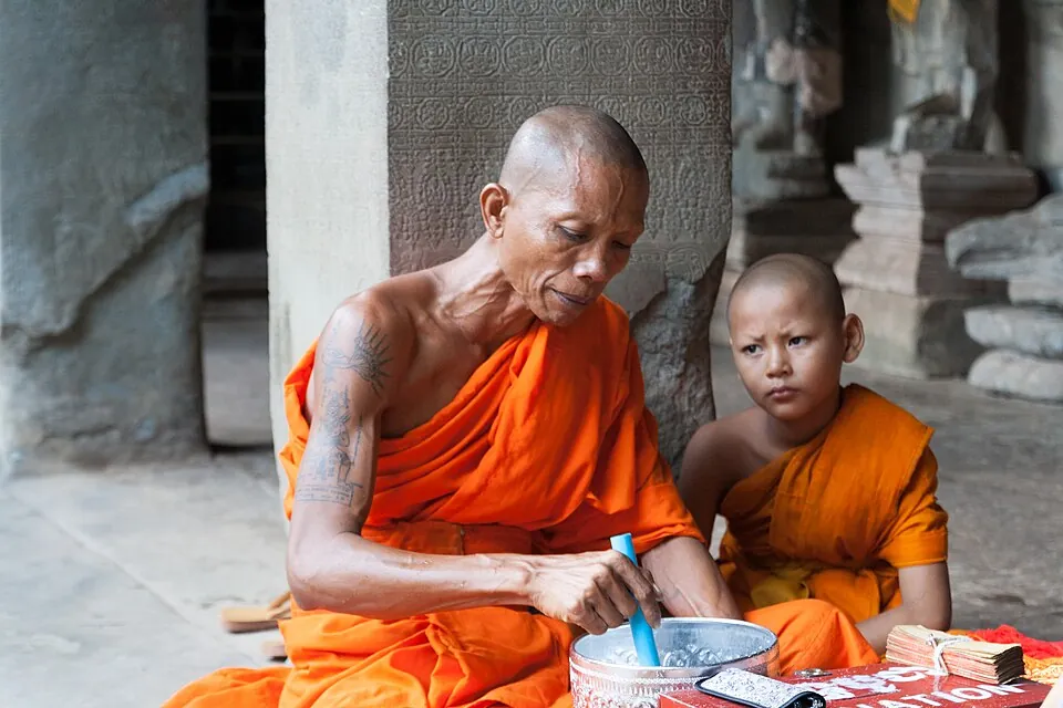 Two Buddhist monks in orange robes beside a carved stone column at Angkor Wat, photographed in 2016