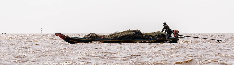 A fisherman travelling in a narrow boat carrying nets on Tonlé Sap